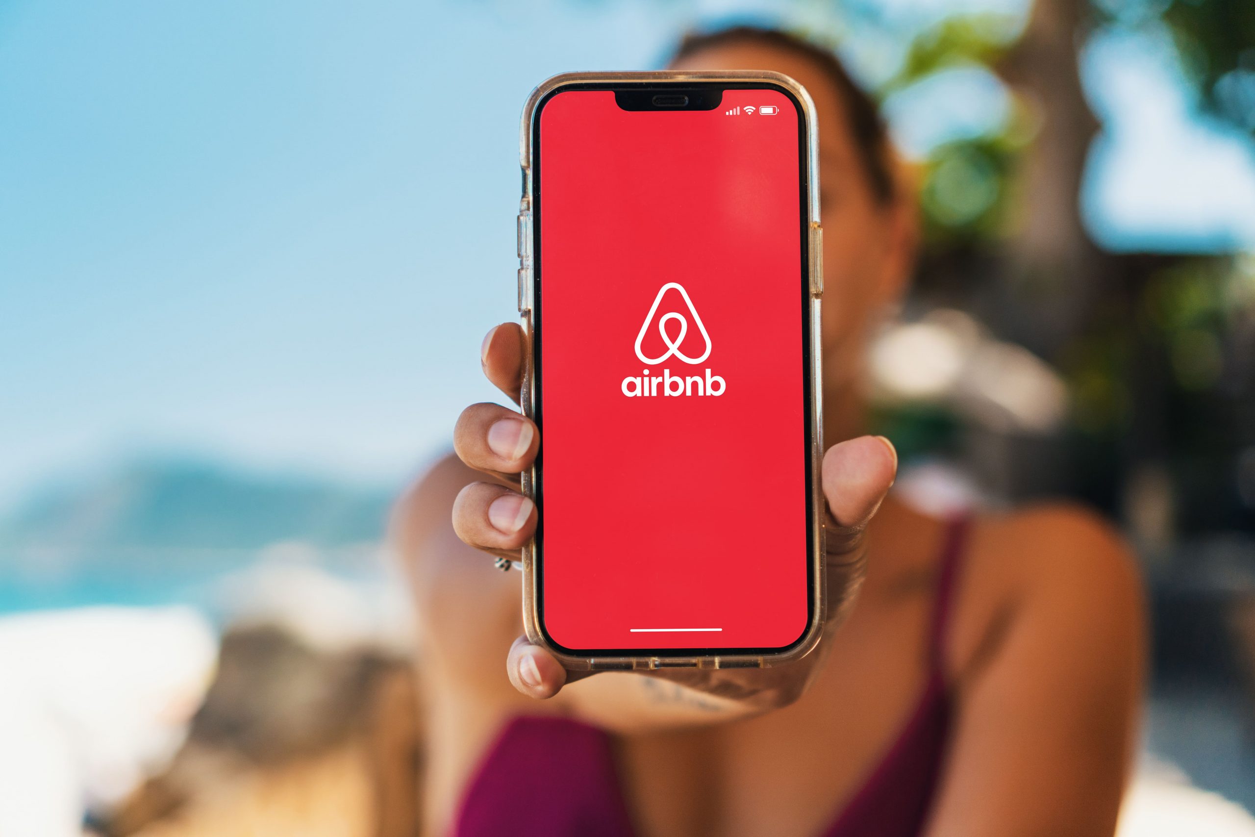 Eine Frau hält ein Handy in die Kamera, auf dem das Airbnb Logo zu sehen ist